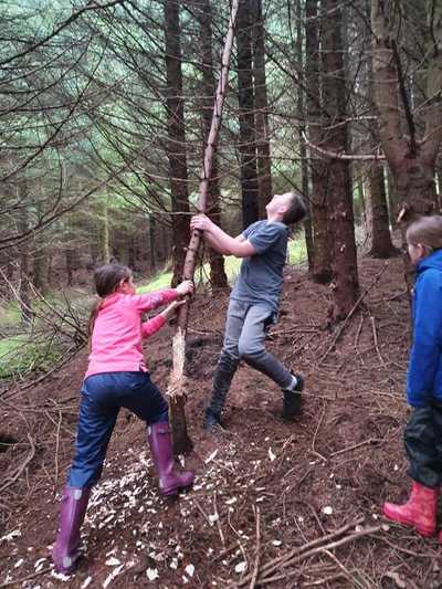 Two children are cutting down a sapling to make a log cabin