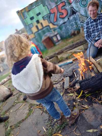 A volunteer sits with a child next to a bonfire toasting marshmallows
